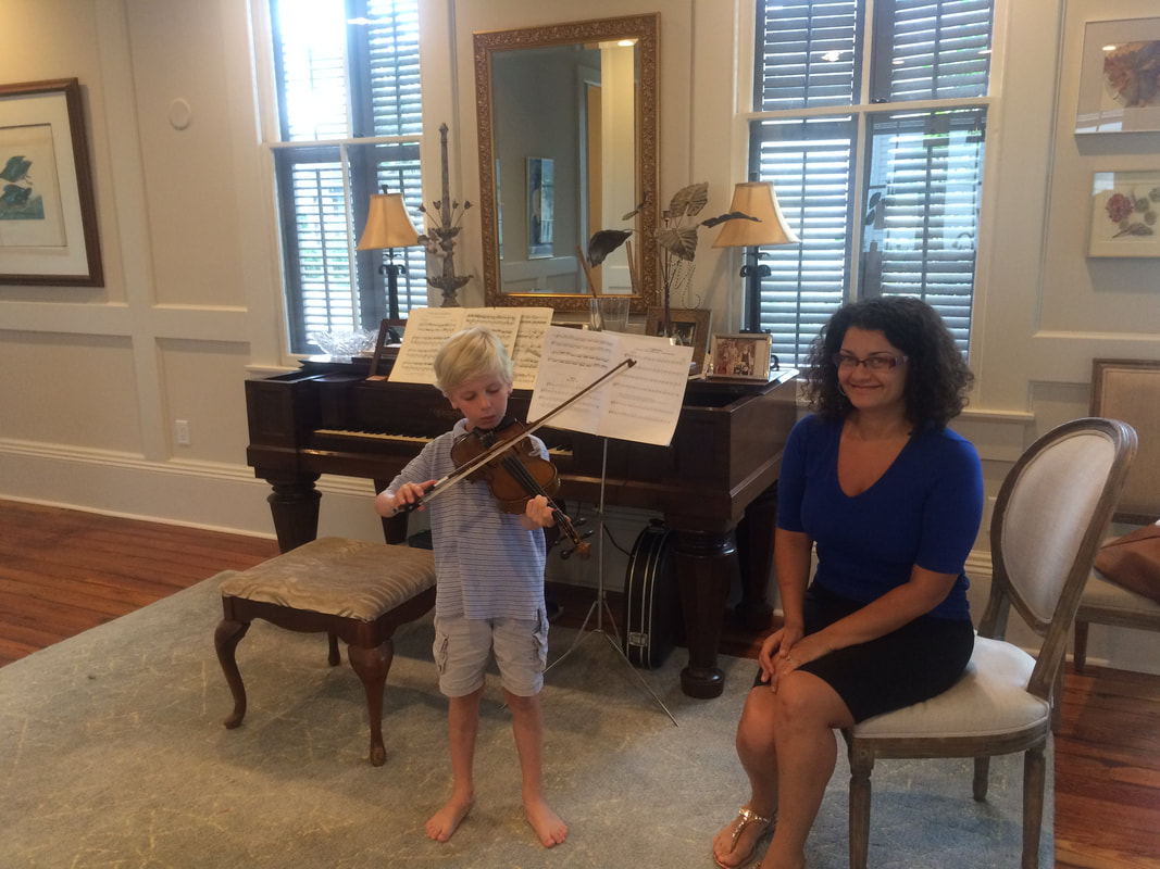 A young boy and woman playing violin in front of a piano.